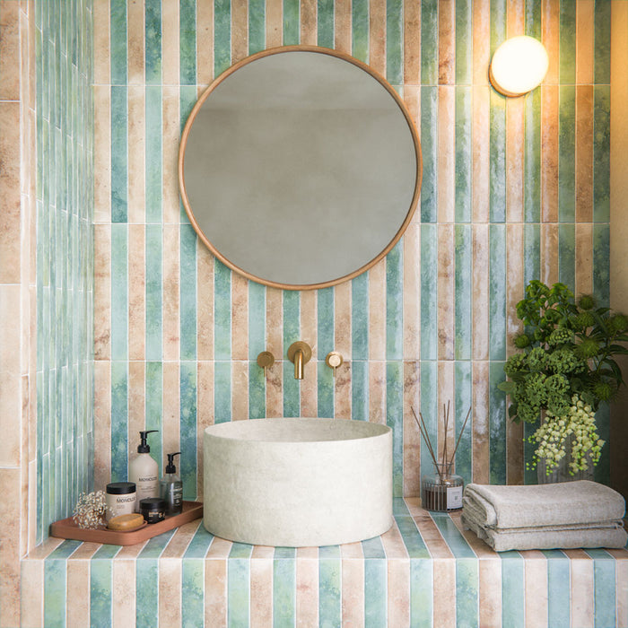 Bathroom setting featuring the Jumairah collection, showcasing slim brick tiles in a vertical striped layout with soft aqua and neutral tones, styled across curved shower walls and a vanity for a serene, spa-inspired finish.