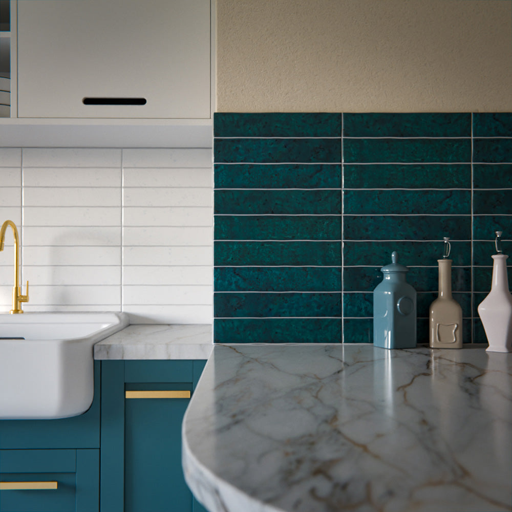Kitchen splashback featuring Bora Bora Amun Blue Brick ceramic wall tiles in a 6.5 × 32.8cm slim brick format with a flux glaze finish, laid horizontally to showcase rich blue-green tonal variation, paired with teal cabinetry, marble-effect worktops, and brass fixtures for a bold, contemporary look.