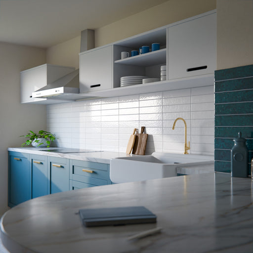 Modern kitchen featuring Bora Bora White Sand Brick ceramic wall tiles in a 6.5 × 32.8cm slim brick format with a flux glaze finish, laid horizontally as a splashback behind blue cabinetry, paired with white worktops, open shelving, and brass tapware for a clean, contemporary look.