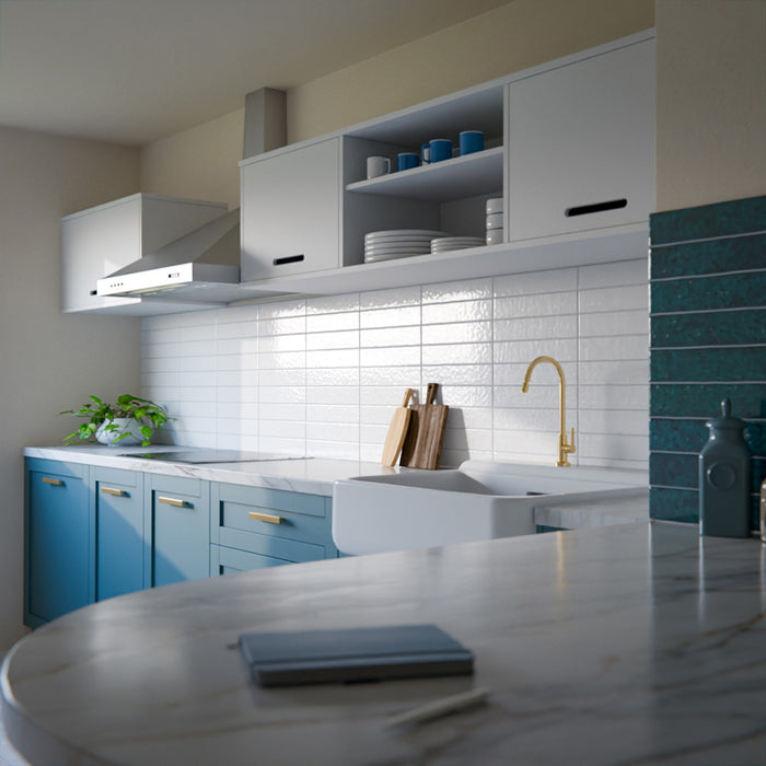 Modern kitchen featuring Bora Bora White Sand Brick ceramic wall tiles in a 6.5 × 32.8cm slim brick format with a flux glaze finish, laid horizontally as a splashback behind blue cabinetry, paired with white worktops, open shelving, and brass tapware for a clean, contemporary look.
