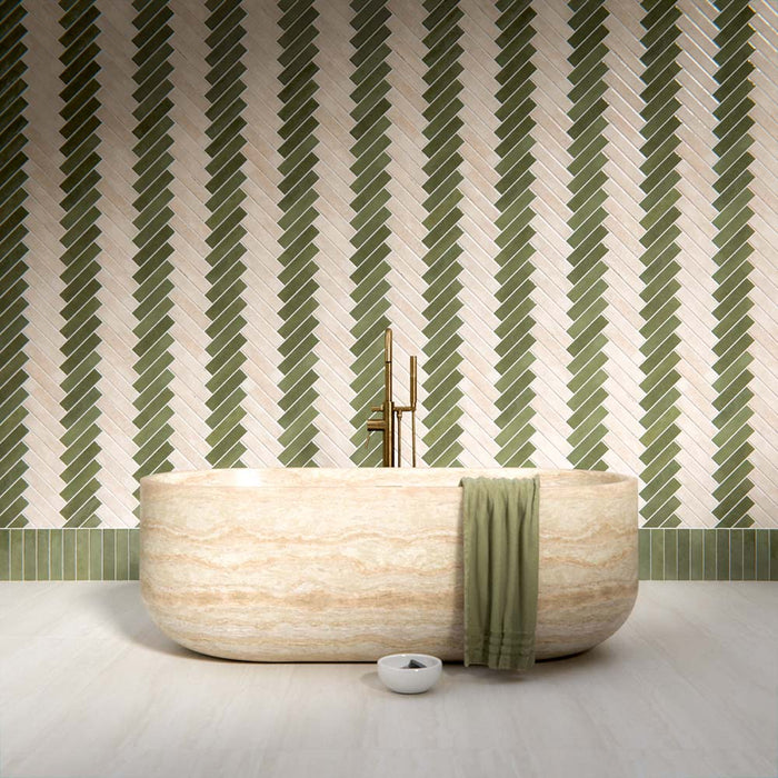 Bathroom interior featuring Nomad Sage Green and Nomad Oatmeal 6 x 24.6cm industrial style brick tiles, arranged in a striking herringbone pattern to create a layered, textural wall design, paired with a natural stone bath and soft neutral flooring for a calm, contemporary finish.