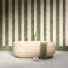 Bathroom interior featuring Nomad Sage Green and Nomad Oatmeal 6 x 24.6cm industrial style brick tiles, arranged in a striking herringbone pattern to create a layered, textural wall design, paired with a natural stone bath and soft neutral flooring for a calm, contemporary finish.