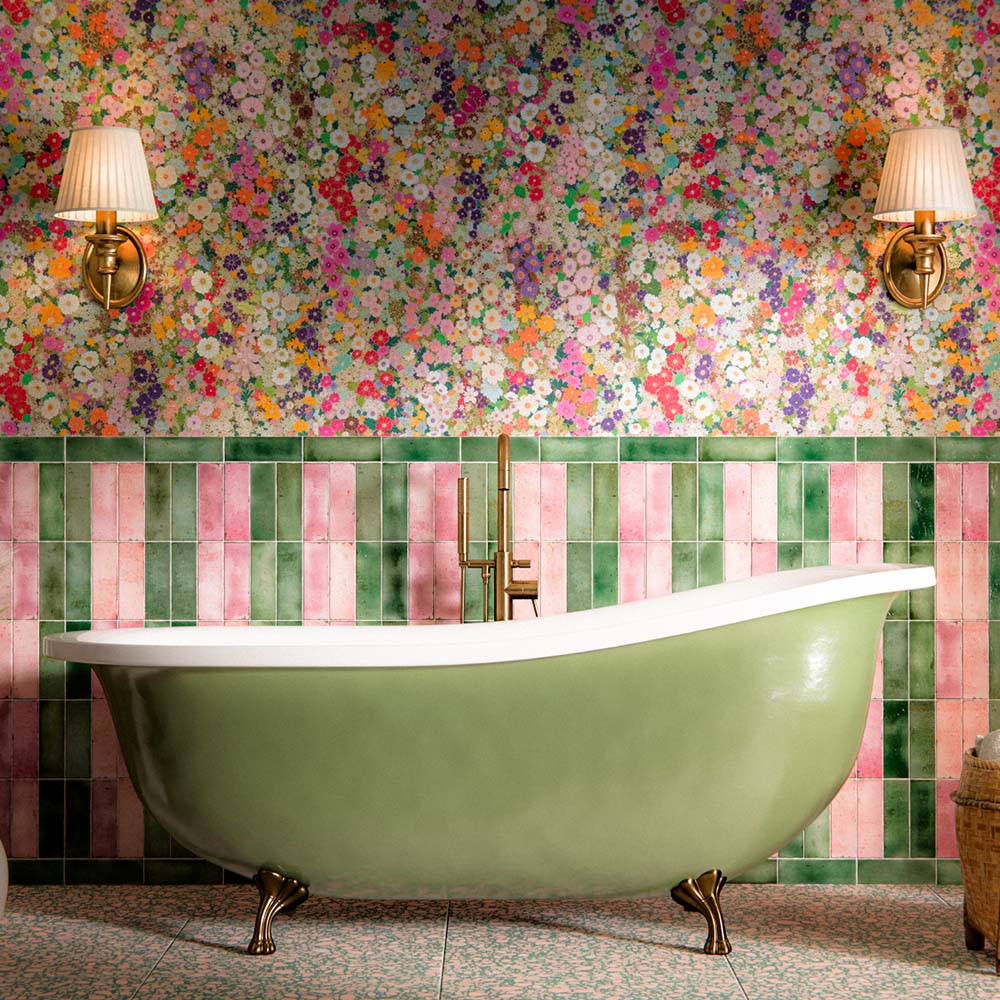 Bathroom interior featuring Foundry Bricks Coral Pink 6.5 x 20cm porcelain wall tiles, installed vertically alongside contrasting green tones to create a playful striped layout, paired with terrazzo effect floor tiles, floral wallpaper, and a freestanding bath for a bold, characterful space.