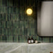Bathroom interior featuring Puzzle Forest Green Brick rectified wall and floor tiles in 5x20cm format, installed vertically as a textured feature wall above large-format marble-effect tiles, styled with brass fittings and modern basin.