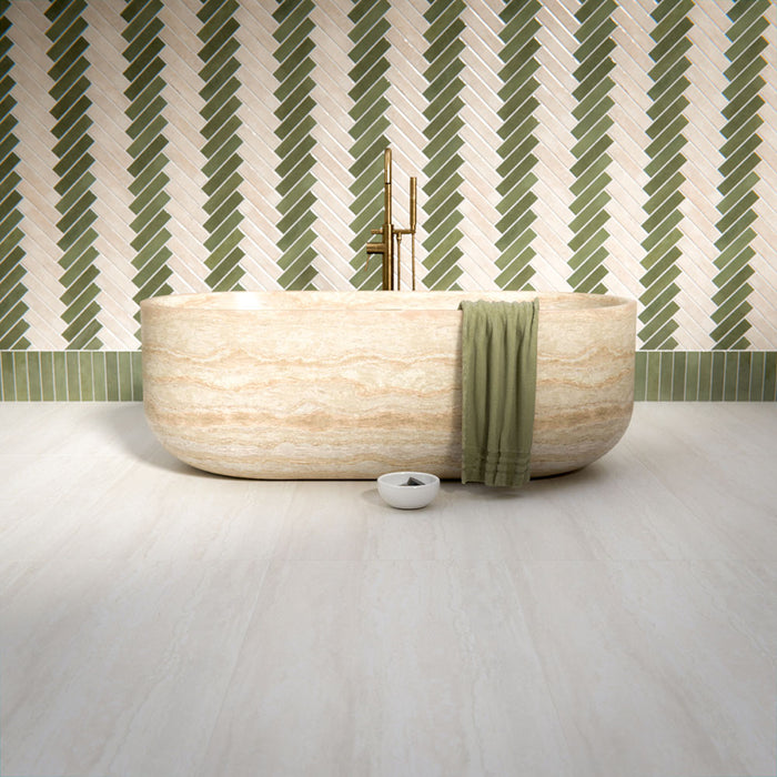 Bathroom interior featuring Nomad Sage Green and Nomad Oatmeal 6 x 24.6cm industrial style brick tiles, arranged in a striking herringbone pattern to create a layered, textural wall design, paired with a natural stone bath and soft neutral flooring for a calm, contemporary finish.