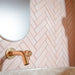 Puzzle Rose Brick Rectified 5x20cm wall and floor tiles laid in a classic herringbone pattern, creating a soft yet striking feature wall. The warm blush tone pairs beautifully with brushed brass fittings and stone-effect surfaces, bringing a refined, contemporary elegance to this bathroom setting.