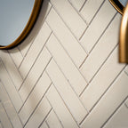 Puzzle White Brick Rectified 5x20cm porcelain tiles styled in a classic herringbone layout, creating a clean and timeless bathroom backdrop. The soft white tone and subtle surface variation add gentle depth while maintaining a crisp, contemporary feel. Paired with brushed brass fittings and a bold marble-effect vanity, the slim brick format enhances texture and pattern, making it ideal for elegant bathroom walls or refined feature areas.