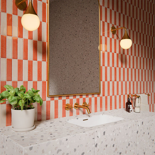 Puzzle Cream Brick Rectified 5x20cm wall and floor tiles in a vertical stacked layout, featuring soft cream tones paired with coral accents in a contemporary bathroom setting with terrazzo vanity and brass fittings.