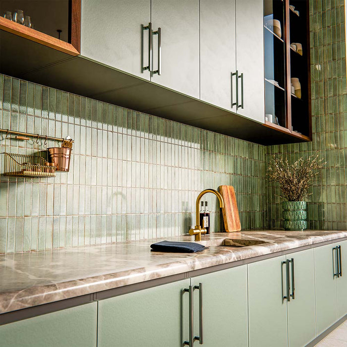 Puzzle Sage Green Brick Rectified 5x20cm porcelain tiles used as a full-height kitchen splashback, showcasing soft sage green tones with subtle speckling and natural shade variation. The slim brick format enhances vertical lines and texture, pairing beautifully with matching cabinetry, warm wood finishes and brass accents for a cohesive, contemporary kitchen design.