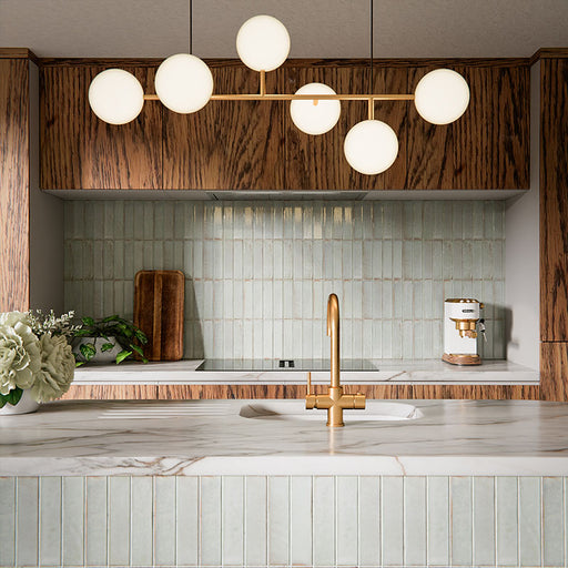Puzzle Breeze Green Brick Rectified 5x20cm porcelain wall and floor tiles styled across a curved kitchen island and splashback, showcasing soft breeze green tones with subtle speckling and gentle shade variation. The elongated brick format enhances the island’s rounded form, while pairing beautifully with warm wood cabinetry, marble worktops and brushed brass fixtures for a calm, contemporary finish.