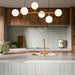 Puzzle Breeze Green Brick Rectified 5x20cm porcelain wall and floor tiles styled across a curved kitchen island and splashback, showcasing soft breeze green tones with subtle speckling and gentle shade variation. The elongated brick format enhances the island’s rounded form, while pairing beautifully with warm wood cabinetry, marble worktops and brushed brass fixtures for a calm, contemporary finish.