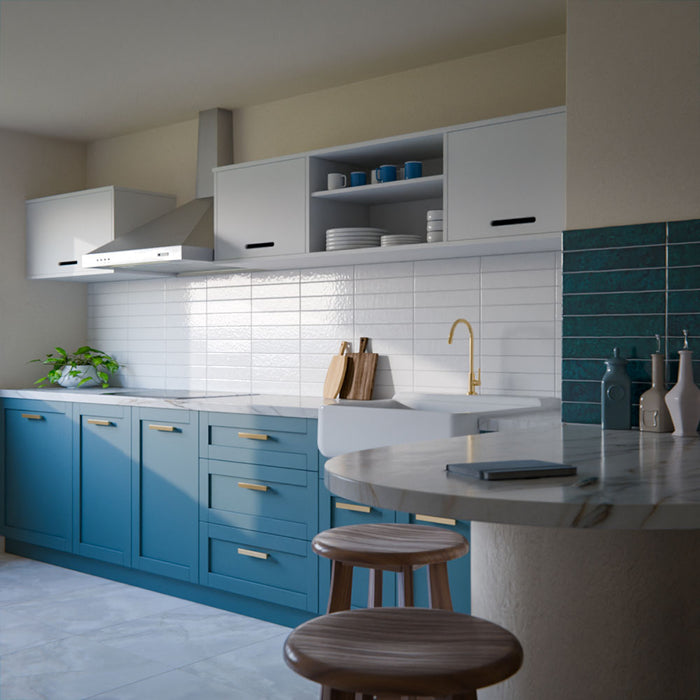Modern kitchen featuring Bora Bora White Sand Brick ceramic wall tiles in a 6.5 × 32.8cm slim brick format with a flux glaze finish, laid horizontally as a splashback behind blue cabinetry, paired with white worktops, open shelving, and brass tapware for a clean, contemporary look.