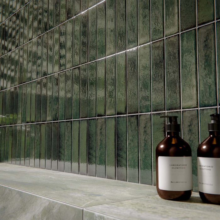 Bathroom interior featuring Puzzle Forest Green Brick rectified wall and floor tiles in 5x20cm format, installed vertically as a textured feature wall above large-format marble-effect tiles, styled with brass fittings and modern basin.