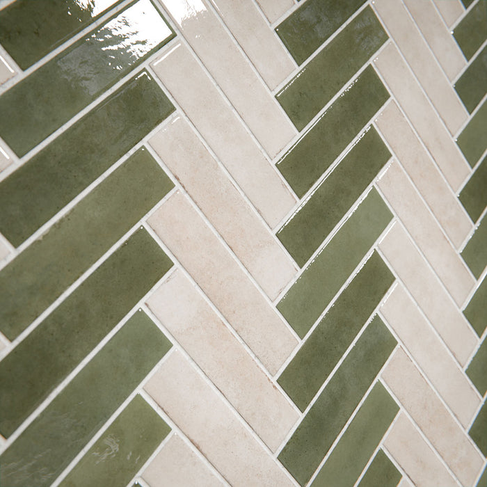 Bathroom interior featuring Nomad Sage Green and Nomad Oatmeal 6 x 24.6cm industrial style brick tiles, arranged in a striking herringbone pattern to create a layered, textural wall design, paired with a natural stone bath and soft neutral flooring for a calm, contemporary finish.