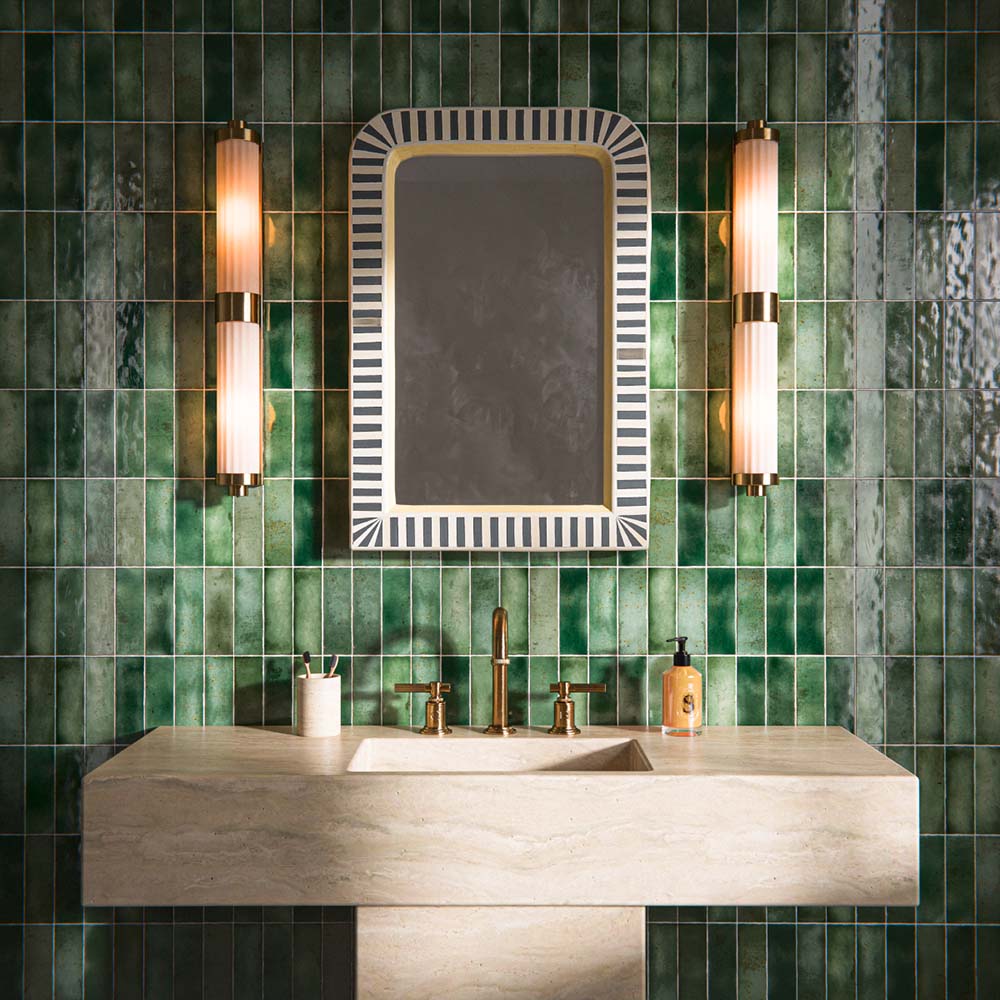 Bathroom interior featuring Foundry Bricks Jade Green 6.5x20cm ceramic wall tiles, arranged in a stacked layout with tonal variation, styled with a stone basin, brass fittings, and a framed mirror with wall lighting.