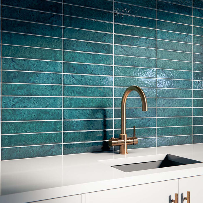 Kitchen interior featuring Bora Bora Amun Blue Brick wall tiles in 6.5x32.8cm format with a flux glaze finish, installed horizontally behind a white worktop and brass tap, showcasing deep blue tonal variation and glossy texture.