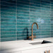 Kitchen interior featuring Bora Bora Amun Blue Brick wall tiles in 6.5x32.8cm format with a flux glaze finish, installed horizontally behind a white worktop and brass tap, showcasing deep blue tonal variation and glossy texture.