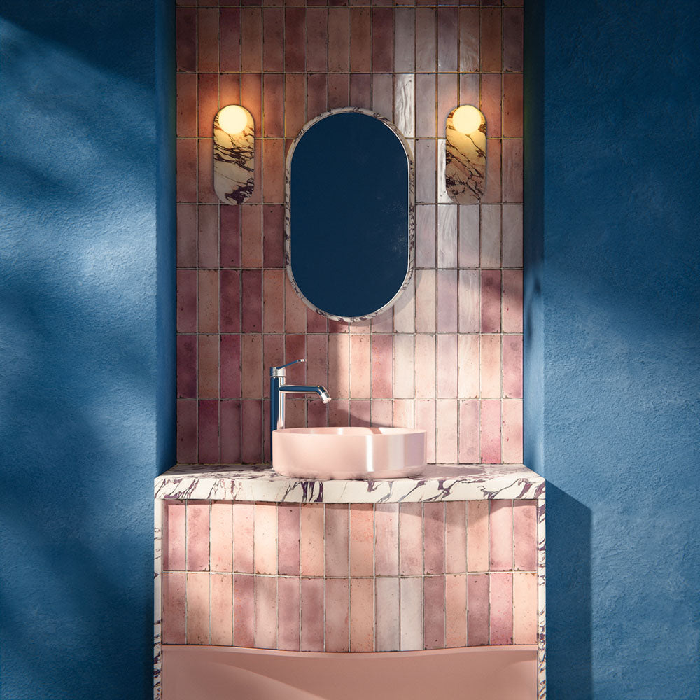 Bathroom interior featuring Foundry Bricks Coral Pink 6.5x20cm ceramic wall tiles in a vertical layout, styled with a curved vanity, blush basin, marble-effect worktop and brushed brass lighting.