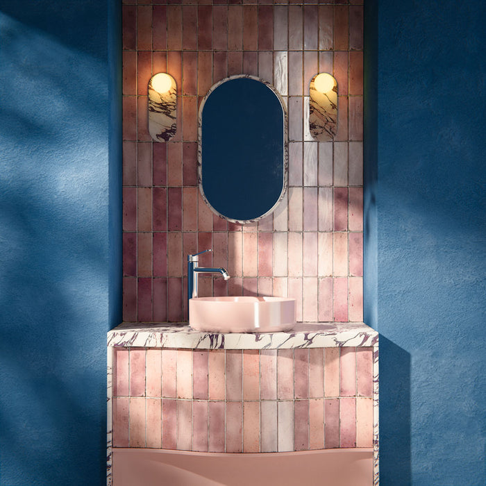 Bathroom interior featuring Foundry Bricks Coral Pink 6.5x20cm ceramic wall tiles in a vertical layout, styled with a curved vanity, blush basin, marble-effect worktop and brushed brass lighting.