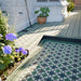 Detail of outdoor steps and patio laid with Greenbrook Manor anti-slip encaustic Victorian-style porcelain tiles, showing the green, black and white geometric pattern with coordinating border tiles beside garden planting.