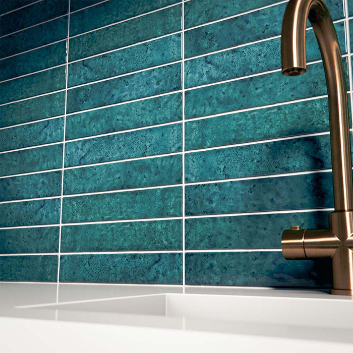 Kitchen interior featuring Bora Bora Amun Blue Brick wall tiles in 6.5x32.8cm format with a flux glaze finish, installed horizontally behind a white worktop and brass tap, showcasing deep blue tonal variation and glossy texture.
