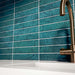 Kitchen interior featuring Bora Bora Amun Blue Brick wall tiles in 6.5x32.8cm format with a flux glaze finish, installed horizontally behind a white worktop and brass tap, showcasing deep blue tonal variation and glossy texture.