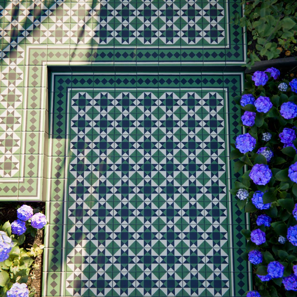 Greenbrook Manor corner 20cm x 20cm porcelain tiles forming a classic Victorian-style green, black and white geometric border around a patterned tiled area, set outdoors beside planting and flowers.
