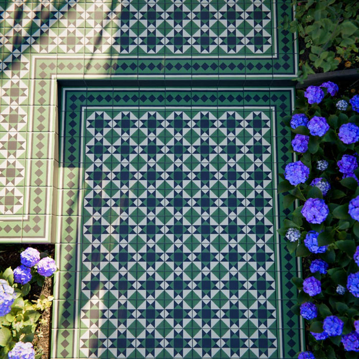 Greenbrook Manor corner 20cm x 20cm porcelain tiles forming a classic Victorian-style green, black and white geometric border around a patterned tiled area, set outdoors beside planting and flowers.