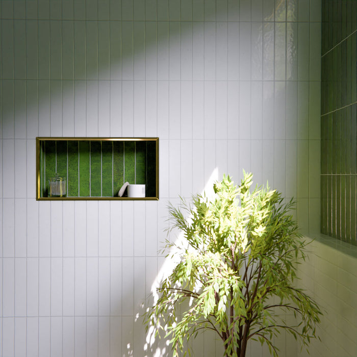Modern bathroom featuring Bora Bora White Sand Brick ceramic wall tiles in a 6.5 × 32.8cm slim brick format with a flux glaze finish, laid vertically and horizontally to create a soft, textured feature wall, paired with a freestanding bath, brass tapware, natural light, and greenery for a calm, spa-like atmosphere.