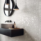 Contemporary bathroom featuring Shards Blanco 3D Terrazzo 60x120cm porcelain wall tiles, showcasing a white terrazzo effect with textured 3D stone chips, paired with a black floating vanity, matte black fittings, round mirror and modern pendant lighting.