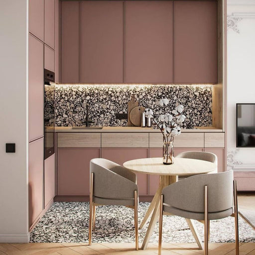 Kitchen featuring Shards Terrazzo Nero Matt 59x118cm porcelain wall and floor tiles in black and white terrazzo-effect tones, styled with blush pink cabinetry, light wood finishes, and contemporary dining furniture.
