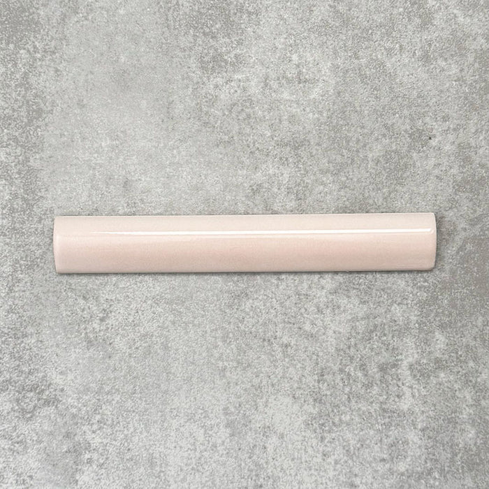 Flat lay of Zellige Pink Mist Bullnose 3 × 20cm Moroccan-style ceramic trim tiles in soft pale pink tones, displayed with a smooth rounded edge and glossy glaze, arranged on a textured grey background to highlight the handcrafted zellige-effect finish and decorative edging profile.