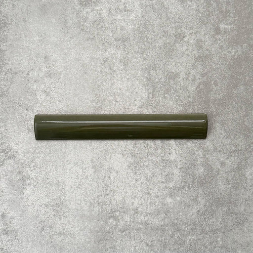 Zellige Botanical Green Bullnose 3 × 20cm Moroccan-style ceramic trim tiles in deep botanical green tones, displayed with a smooth rounded edge and glossy glaze, arranged on a textured grey background to highlight the handcrafted zellige-effect finish and decorative edging profile.