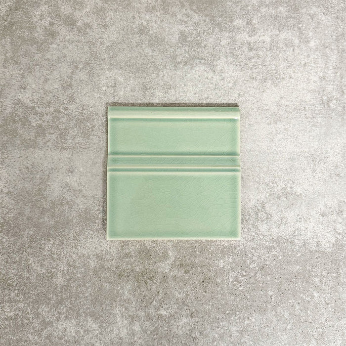 Close-up of Pimlico Lime Green 15 × 15cm ceramic skirting tile with a crackle glaze finish, showcasing soft green tones and moulded detailing designed to neatly finish the edge between walls and floors.