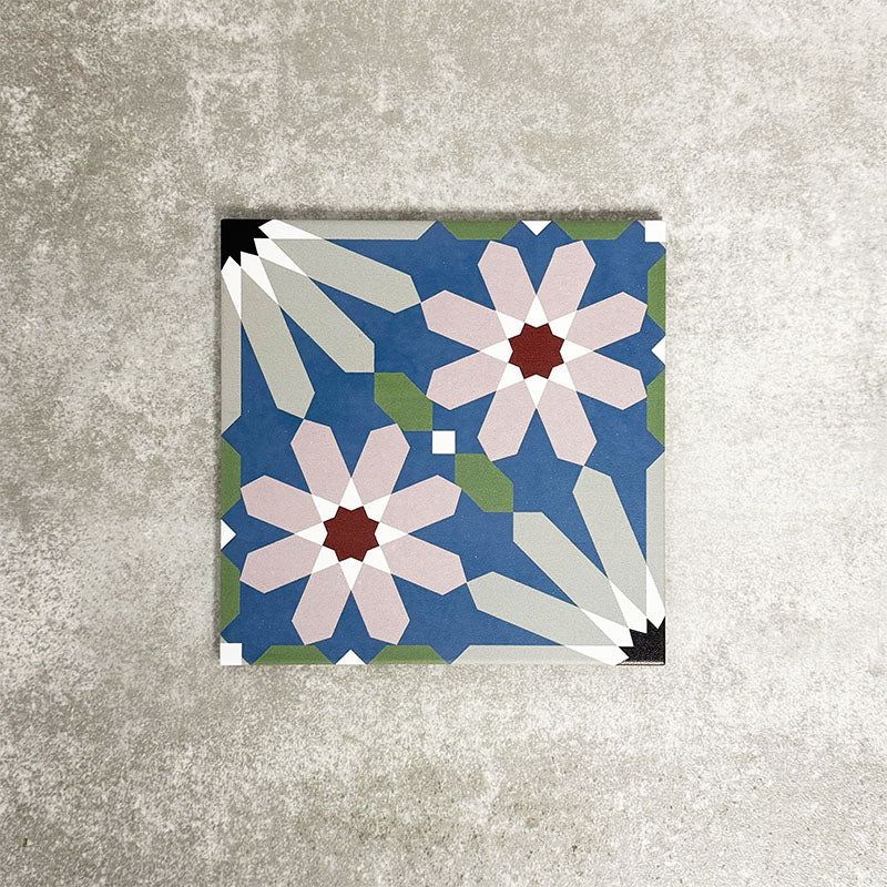 Single Fez Artisan 20x20cm Moroccan-style porcelain tile displayed against a textured grey background, highlighting the multicolour geometric design with soft blue, blush pink, green and terracotta star motifs in an encaustic-inspired pattern.