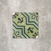 Single Balthazar Verde 20×20cm Moroccan-style porcelain tile displayed against a neutral stone-effect background, highlighting the intricate geometric pattern in layered green tones with contrasting dark accents and a traditional encaustic-inspired matt finish.