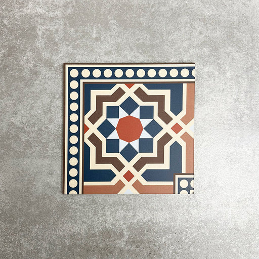 Single Balthazar Grand Corner 20×20cm porcelain tile displayed against a neutral stone-effect background, featuring a Moroccan-inspired geometric corner border design in deep blue, warm brown, terracotta and cream tones, designed to frame patterned layouts with a cohesive, decorative finish.