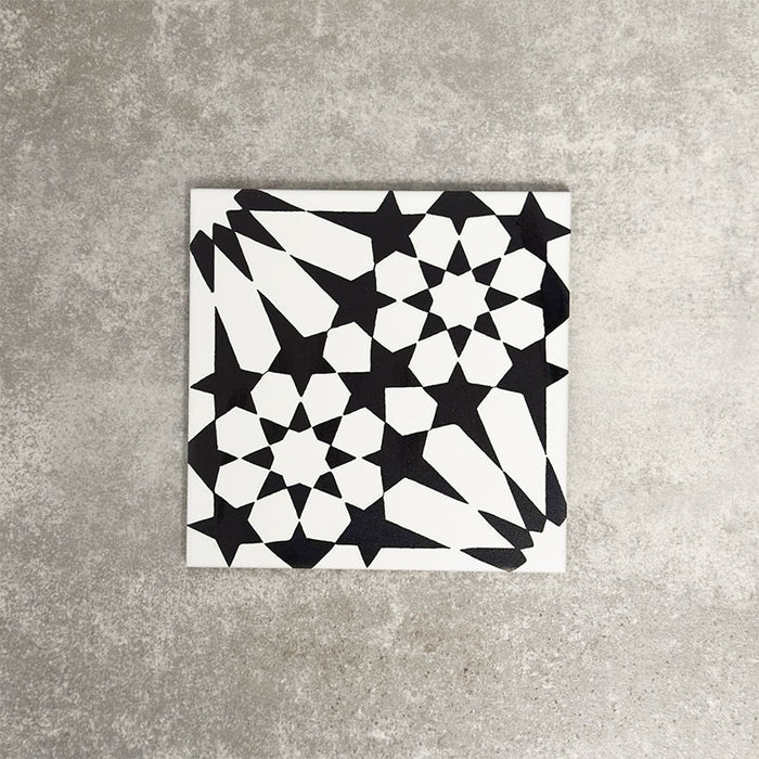 Fez Winter Moroccan-style porcelain tile shown as a single tile sample. The 20 × 20cm tile features a bold black and white geometric star pattern inspired by traditional Moroccan designs, with sharp contrast and crisp lines. The encaustic-effect finish highlights the intricate detailing, making it ideal for statement floors, splashbacks or feature walls in both modern and classic interiors.