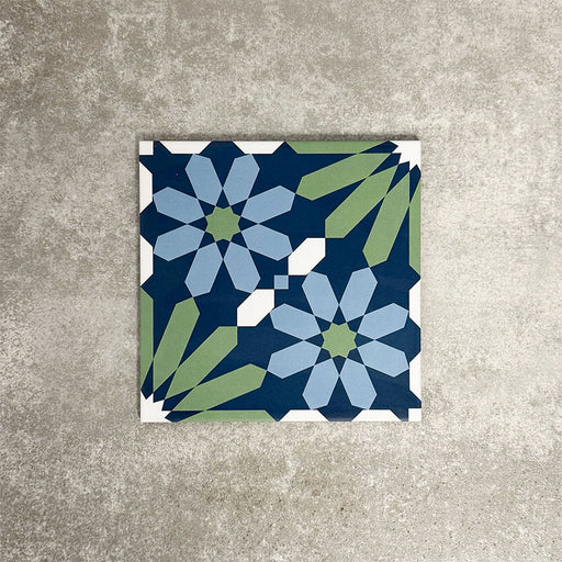 Single Fez Springs 20x20cm Moroccan-style porcelain tile displayed against a textured grey background, highlighting the geometric floral design in layered navy, blue and soft green tones with an encaustic-inspired finish.