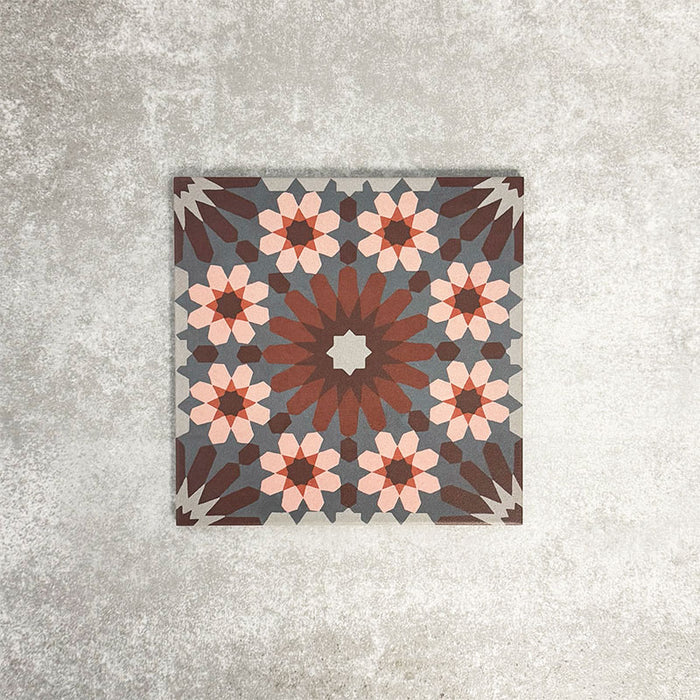Fez Rosso Moroccan-style porcelain tile shown as a single 20 × 20cm tile, highlighting the intricate geometric pattern in full detail. Deep terracotta and earthy red tones radiate from the centre, layered with soft blush pink star motifs and set against a muted grey background. The balanced, symmetrical design draws inspiration from traditional Moroccan tilework while the porcelain finish keeps it practical and durable. A bold yet elegant choice.