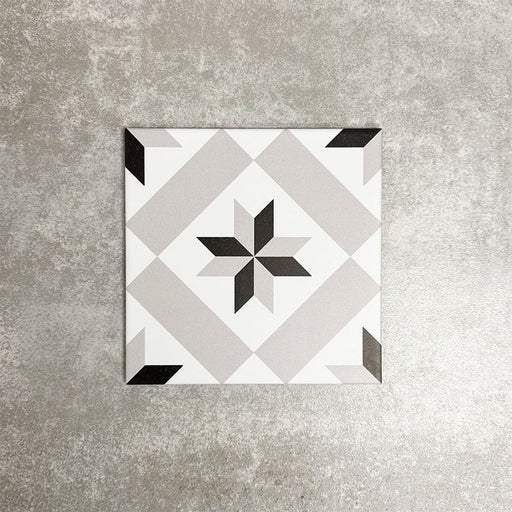 Single Canterbury Star Victorian-style porcelain tile in a 20 × 20cm format, featuring a central star motif in soft grey and black tones on a light background, shown on a neutral surface to highlight the classic geometric design suitable for wall and floor use.