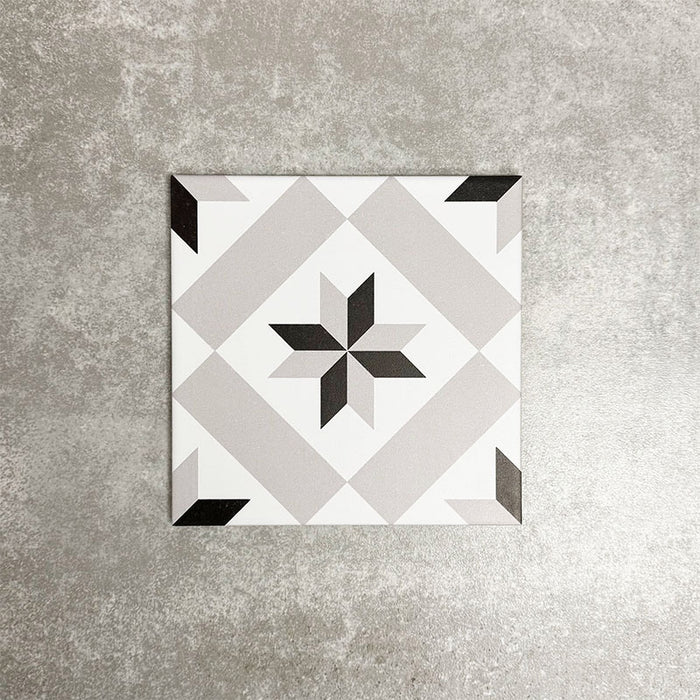 Single Canterbury Star Victorian-style porcelain tile in a 20 × 20cm format, featuring a central star motif in soft grey and black tones on a light background, shown on a neutral surface to highlight the classic geometric design suitable for wall and floor use.
