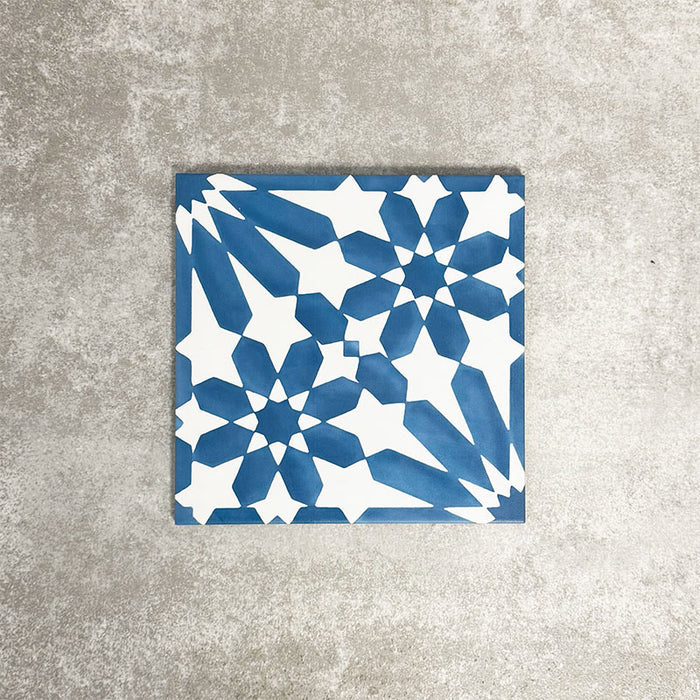 Single Fez Azure Blue 20x20cm Moroccan-style porcelain tile displayed against a textured grey background, highlighting the crisp blue and white geometric star pattern with an encaustic-inspired design.