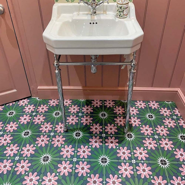 Bathroom floor featuring Fez Autumn 20x20cm Moroccan-style porcelain tiles, with an intricate geometric floral pattern in deep green, blush pink and dark accents, styled beneath a classic white pedestal sink and soft pink wall panelling.