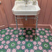 Bathroom floor featuring Fez Autumn 20x20cm Moroccan-style porcelain tiles, with an intricate geometric floral pattern in deep green, blush pink and dark accents, styled beneath a classic white pedestal sink and soft pink wall panelling.