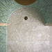 Walk-in shower featuring Essentials Terrazzo Stone Avorio 60x120cm terrazzo effect porcelain wall and floor tiles, paired with green glazed brick wall tiles, arched ceiling detail, and a brushed brass shower drain.