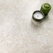 Kitchen surface featuring Essentials Terrazzo Stone Blanca 60x120cm terrazzo effect porcelain tiles, styled with a ceramic candle and green glass vessel, highlighting soft white and beige stone-inspired variation.