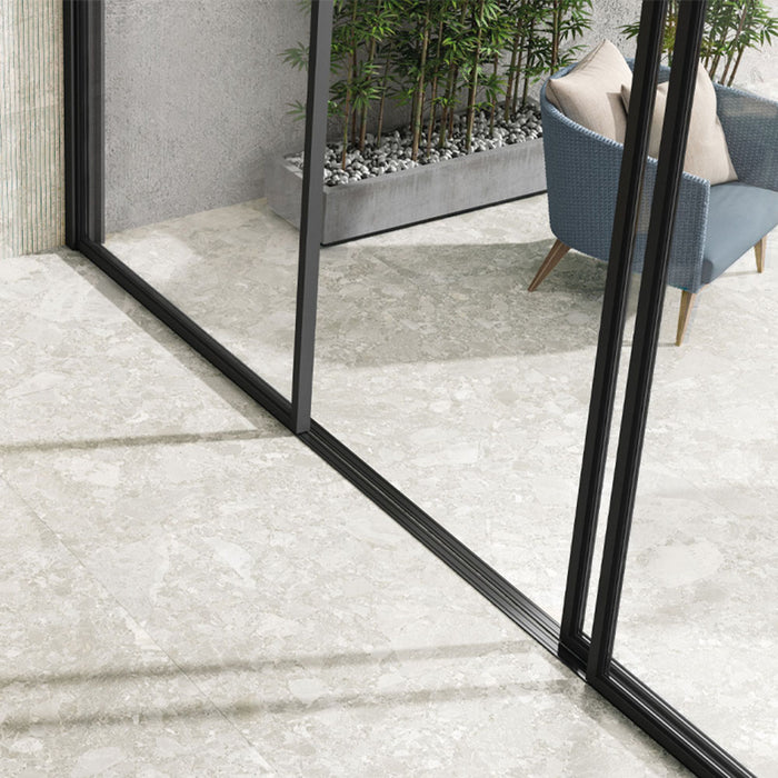 Indoor-outdoor space featuring Essentials Terrazzo Stone Blanca 60x120cm terrazzo effect porcelain floor tiles, paired with sliding glass doors, a woven lounge chair, and planted greenery for a seamless, light-filled finish.