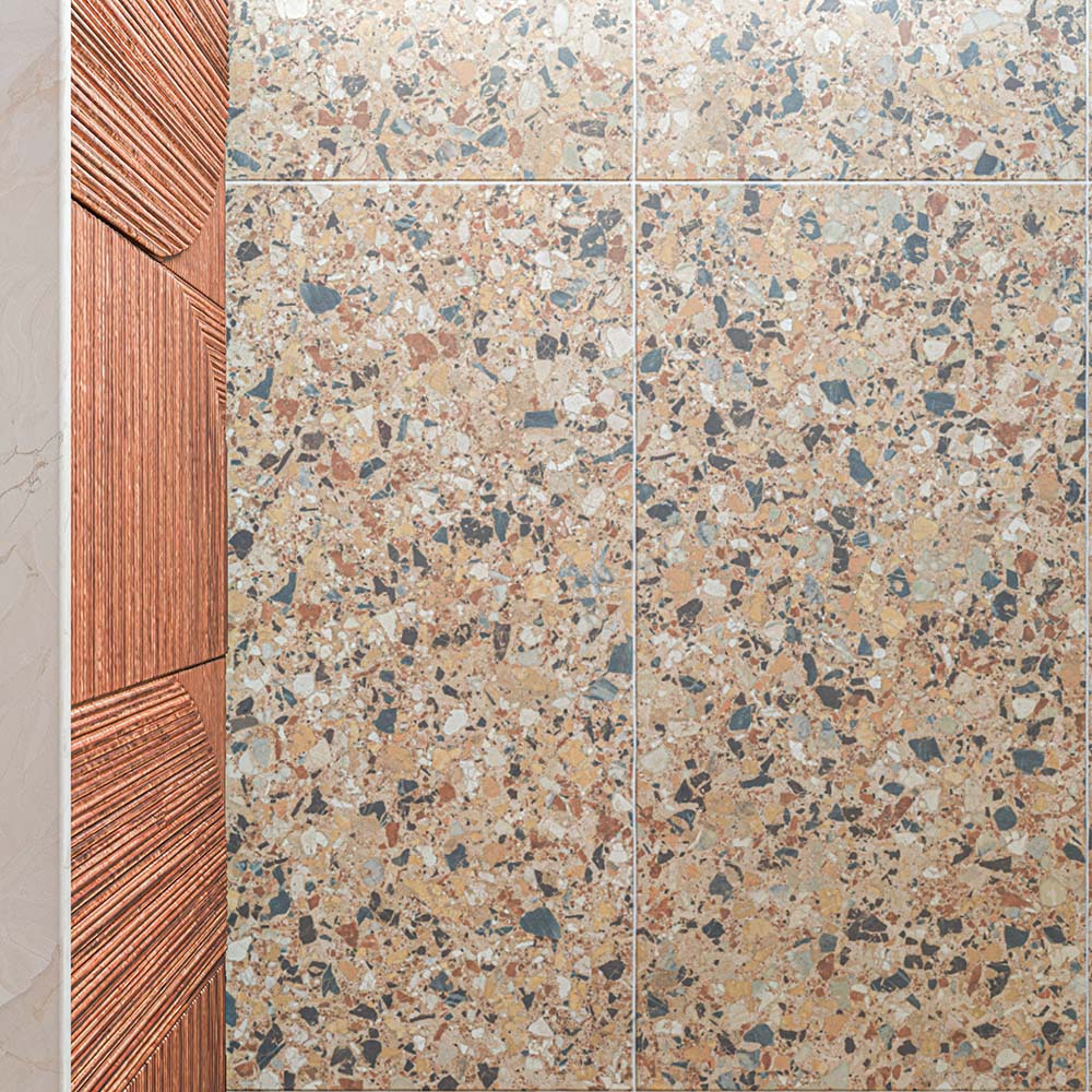 Stuzzi Amber 60cm x 120cm terrazzo effect tiles with a 4D brushed finish, highlighting the detailed mix of warm amber, terracotta, cream and contrasting darker fragments.