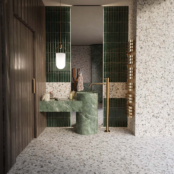 Bathroom featuring Stuzzi Lunar 60x60cm classical terrazzo style porcelain tiles with a 4D brushed finish, paired with deep green fluted wall tiles, green marble effect basins, brushed brass fittings and dark wood panelling for a luxurious contemporary interior.